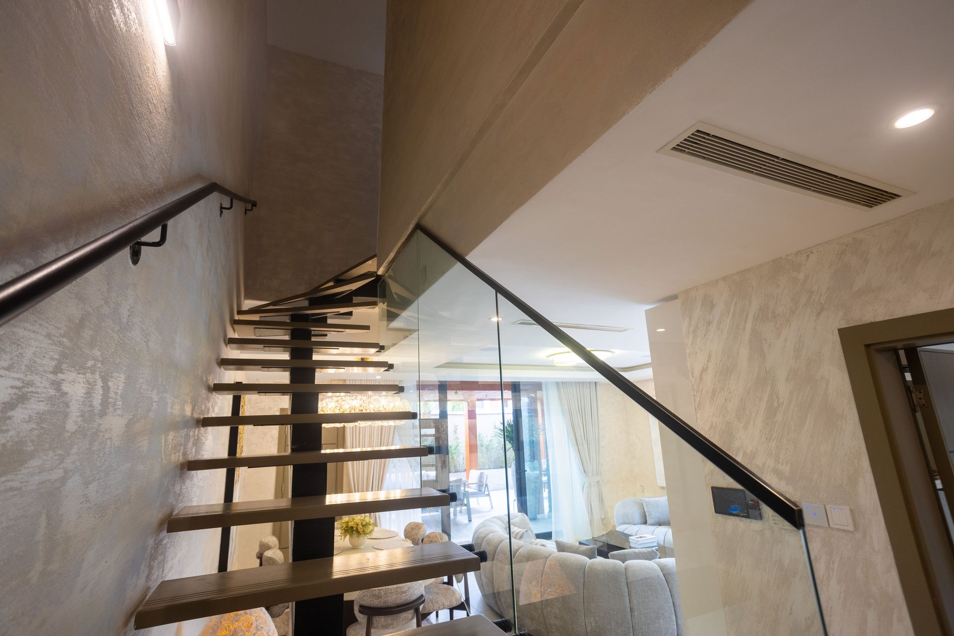 Staircase with open wooden steps and black railings in a modern interior, leading to a bright living area