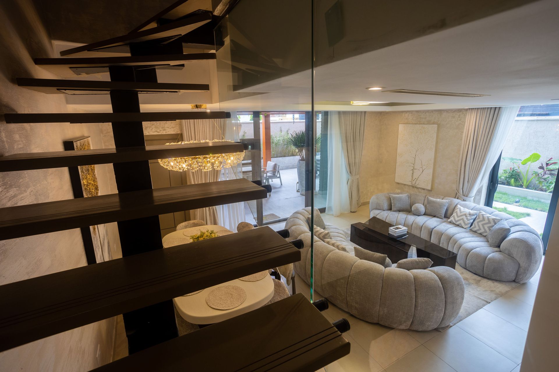 Modern living room with curved gray sofas, large mirror, and dark wooden staircase rails