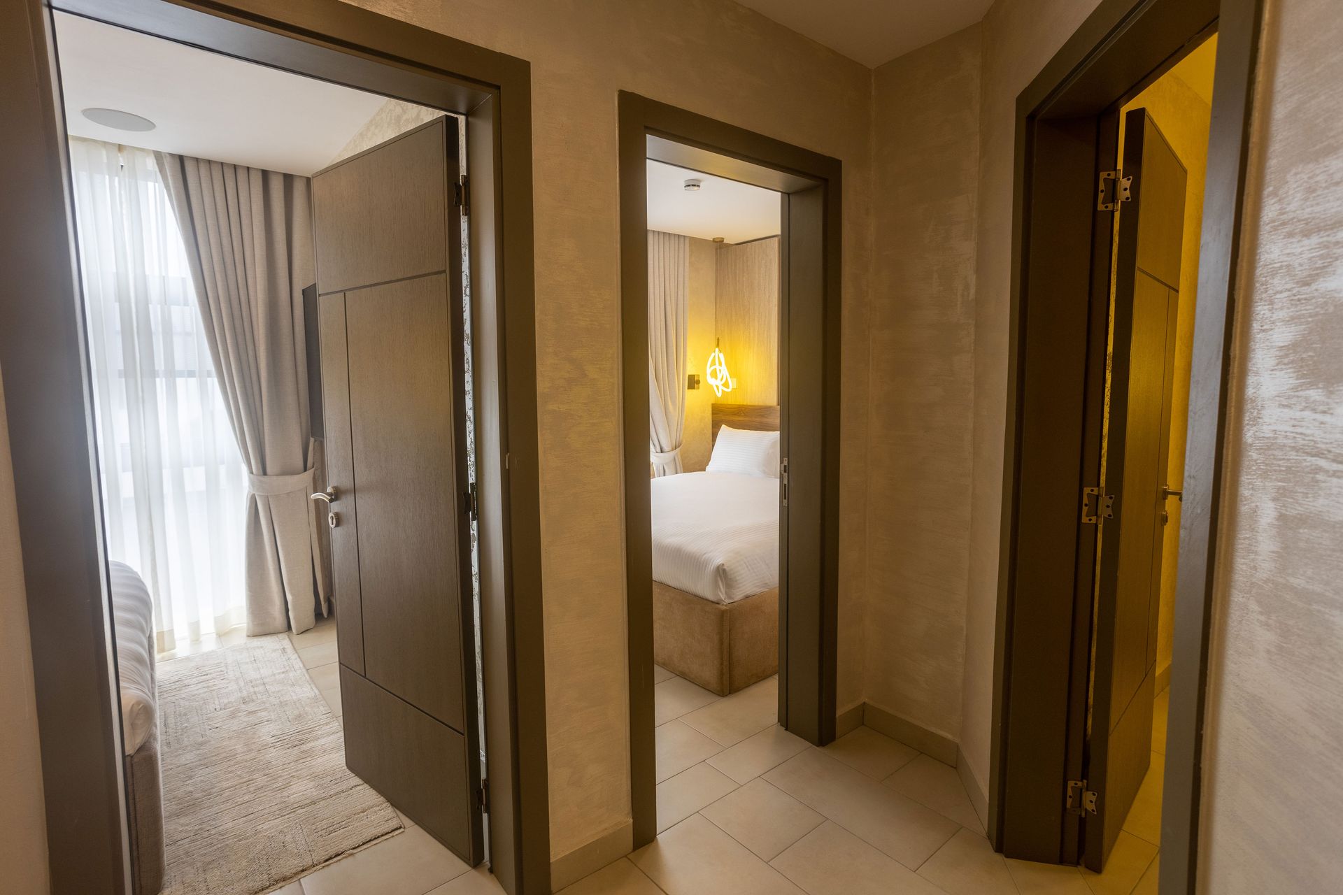 Hallway with open doors to a bedroom, bathroom, and closet in a beige apartment interior