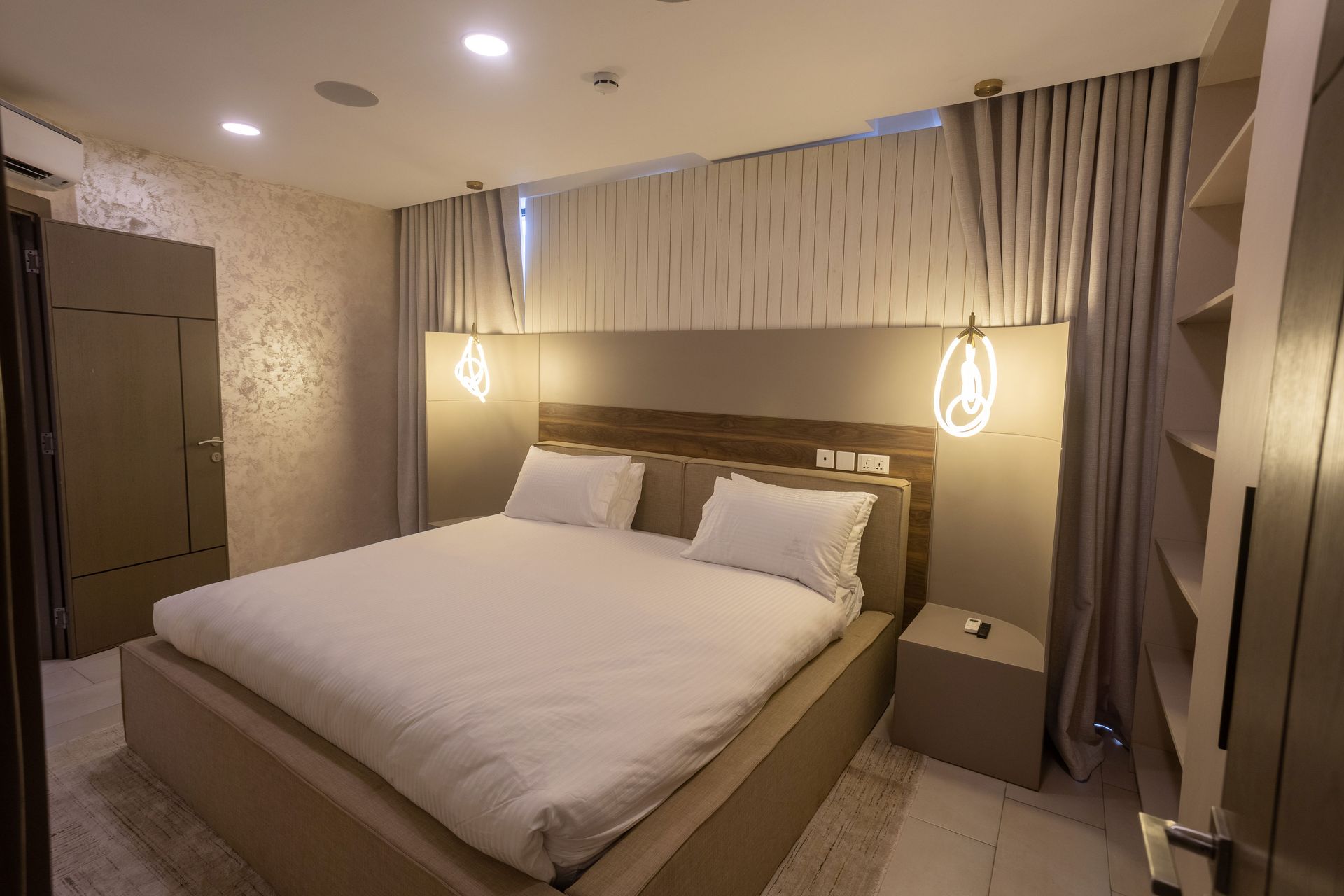 Modern bedroom with a large bed, hanging pendant lights, and neutral beige decor