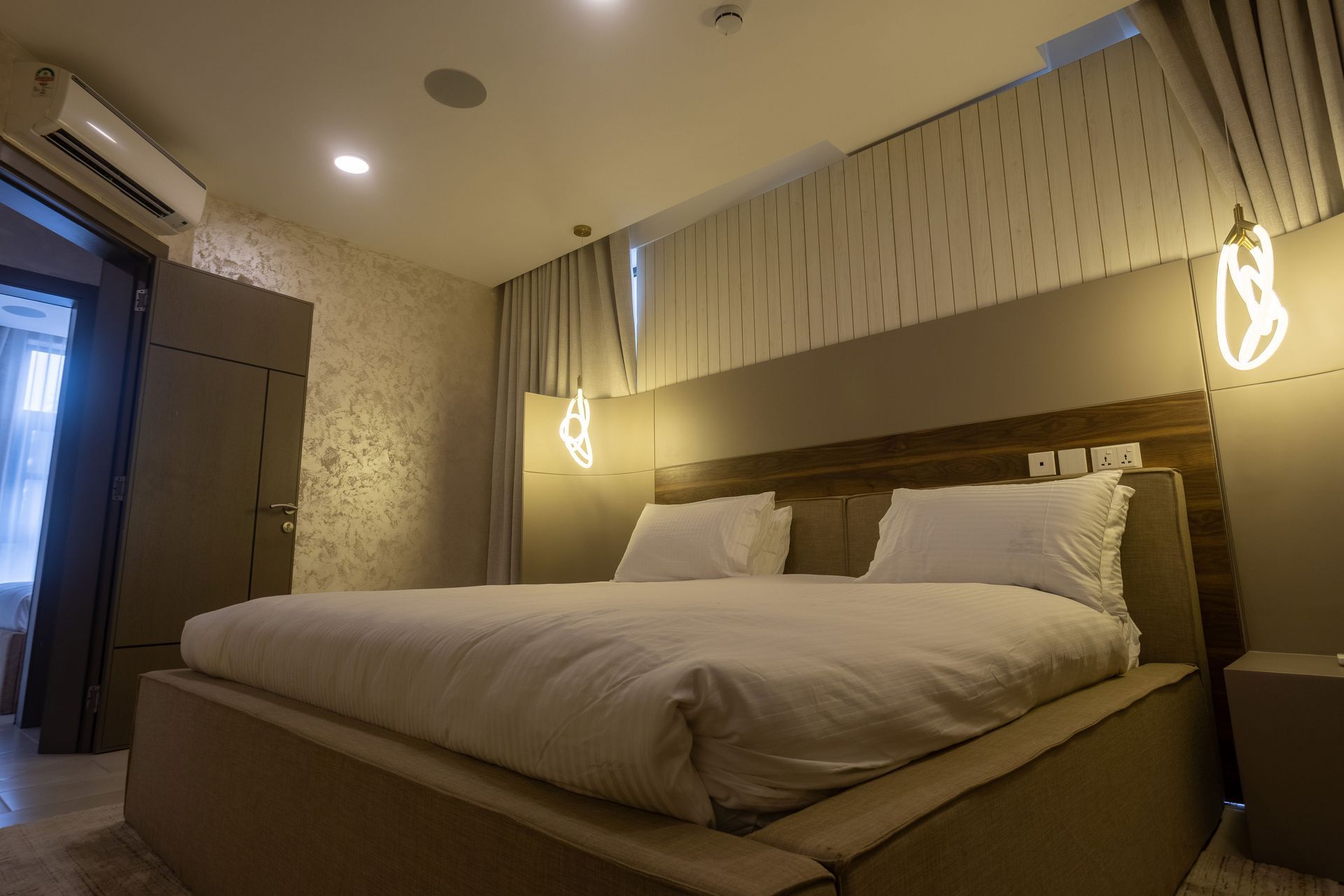 Modern hotel bedroom with large bed, warm lighting, and textured walls