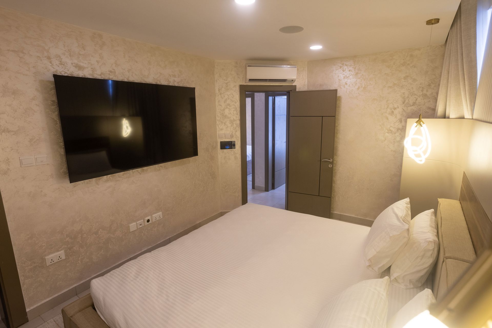 Modern hotel room with a bed, wall-mounted TV, and open door to the hallway