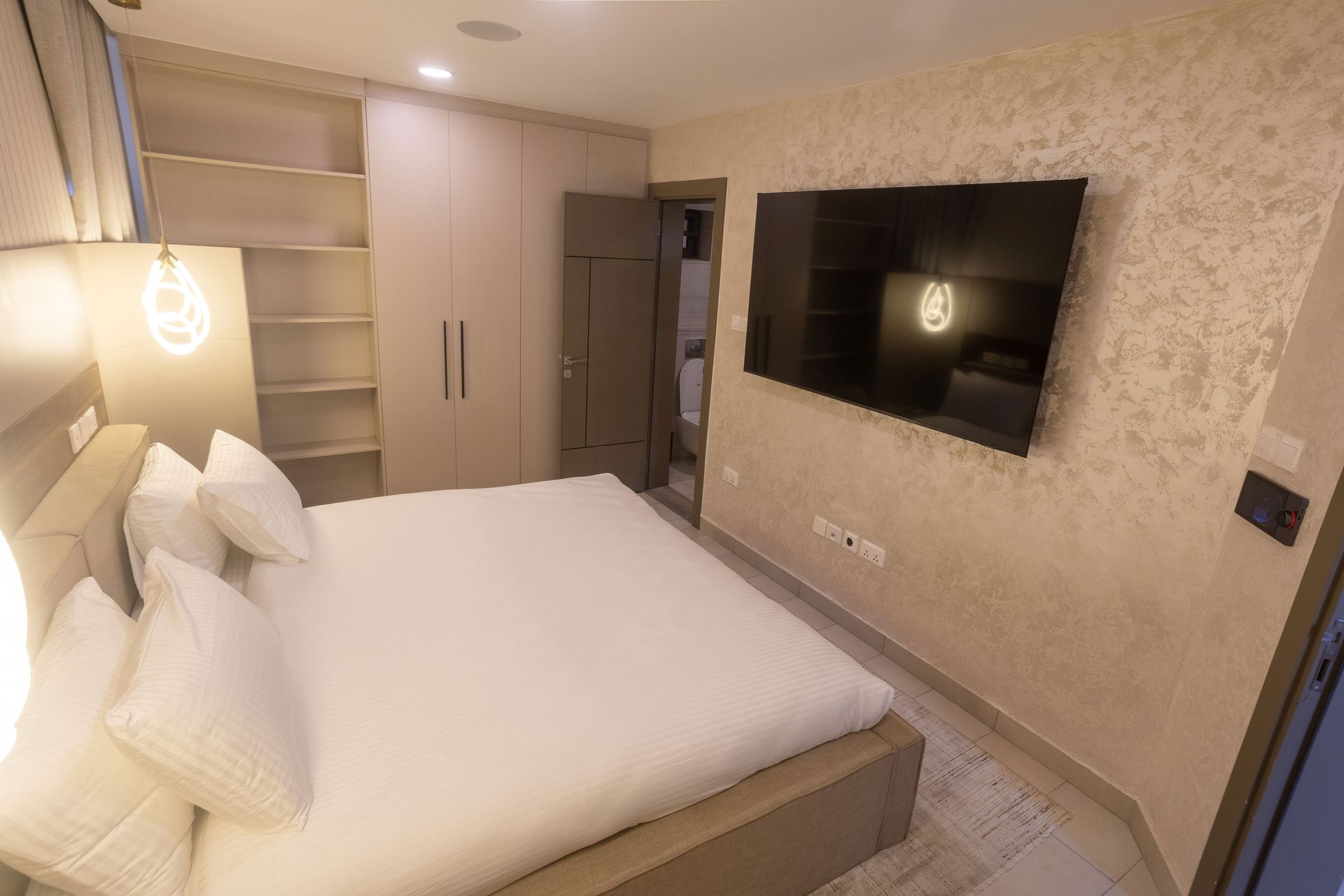 Modern bedroom with a white bed, built-in shelves, wardrobe, and wall-mounted TV.
