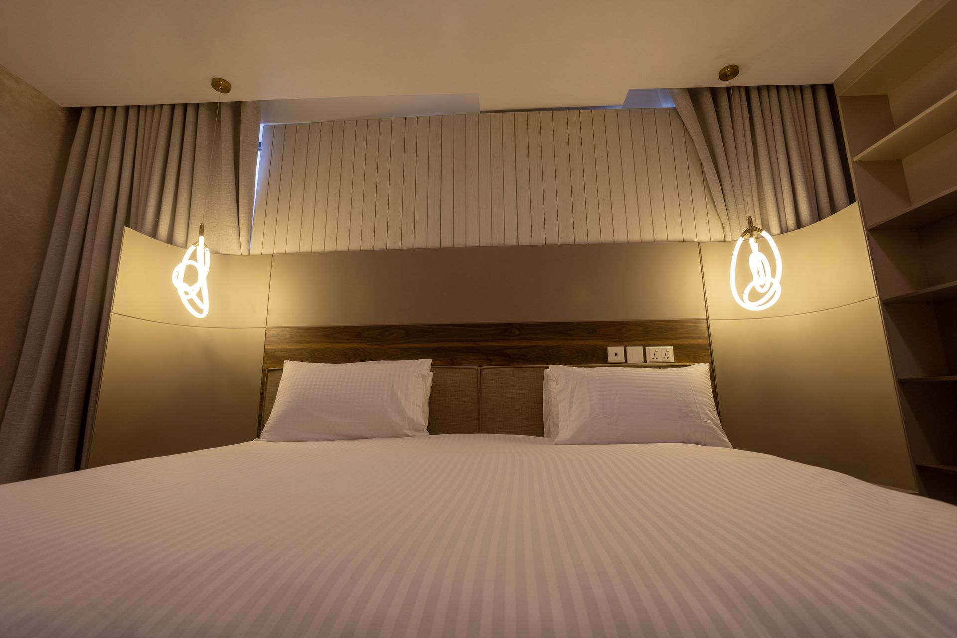 Cozy hotel bed with white linens, warm wall lights, and curtains on either side