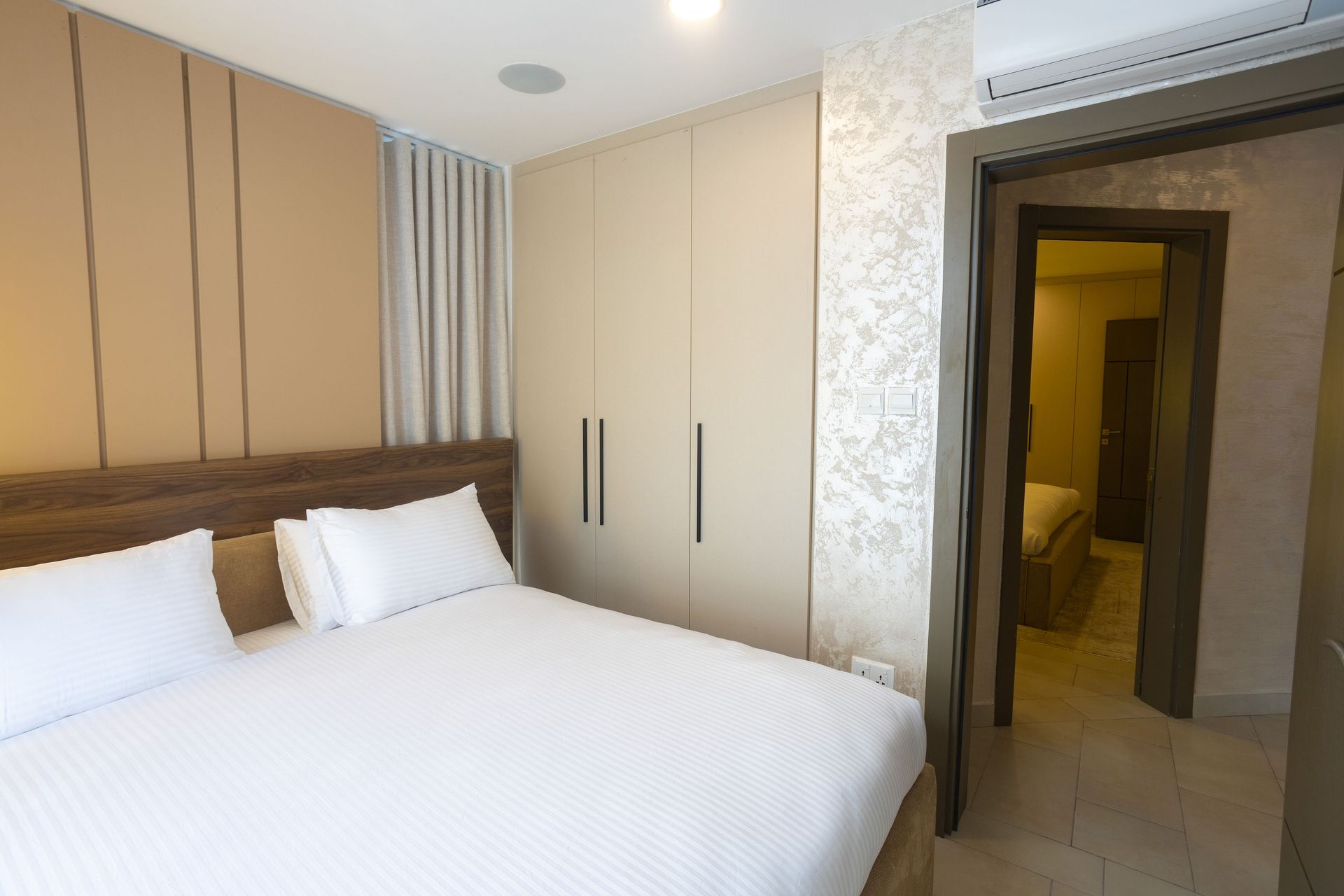 Modern bedroom with a white bed, beige wardrobe, and an open doorway to a hallway