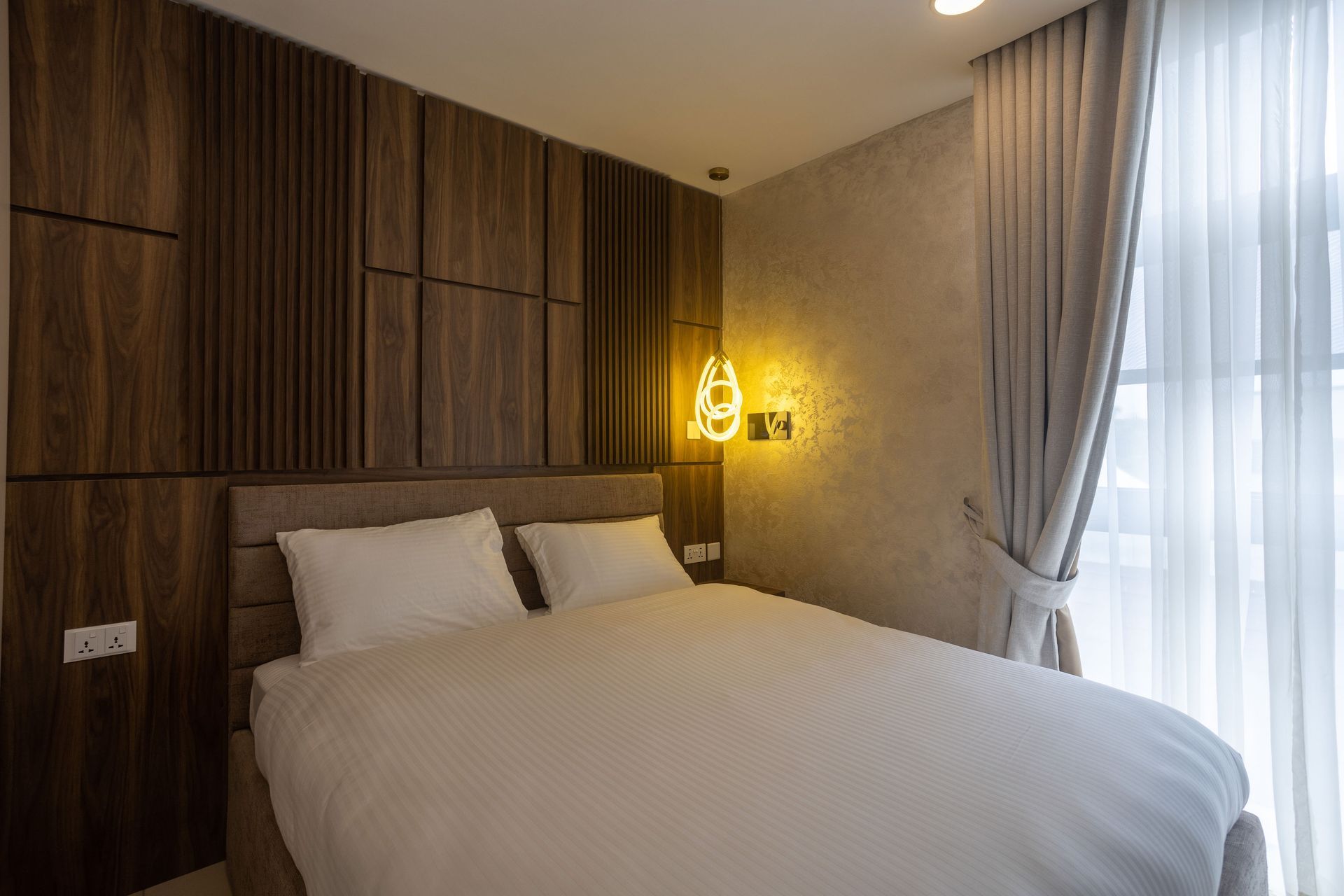 Cozy bedroom with a large bed, wood-paneled wall, warm lamp, and curtains by a bright window