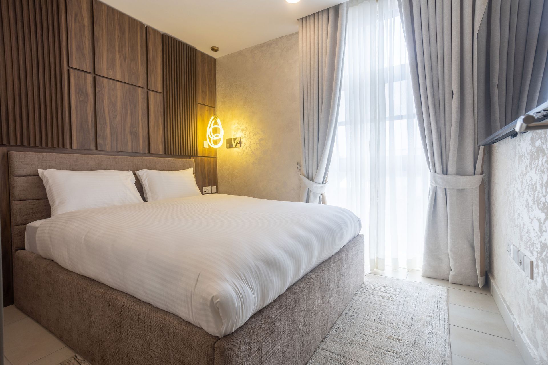 Modern bedroom with a large bed, wood panel wall, and bright sheer curtains by a window