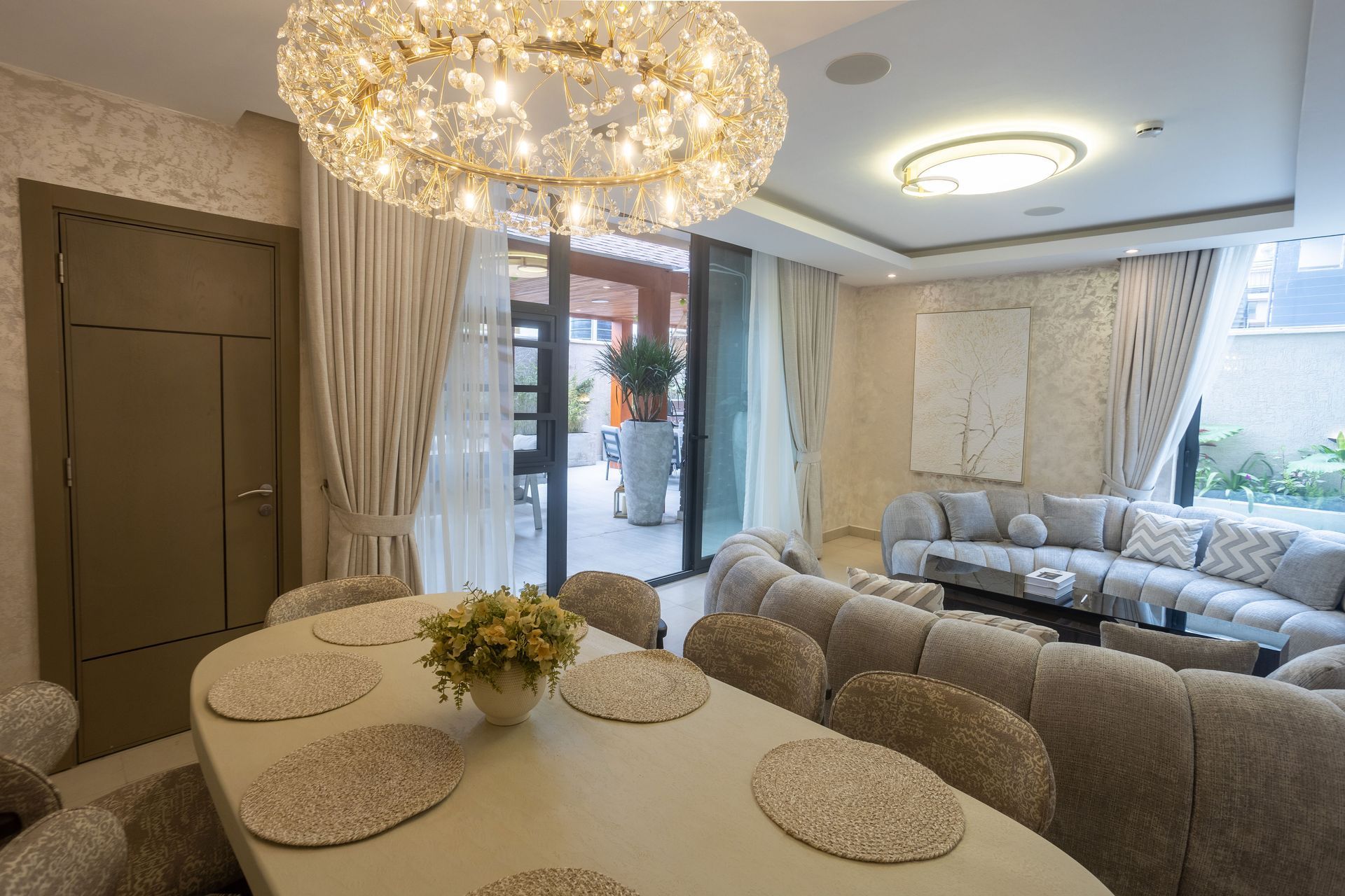 Elegant dining and living room with crystal chandeliers, round table, sofa, and balcony doors