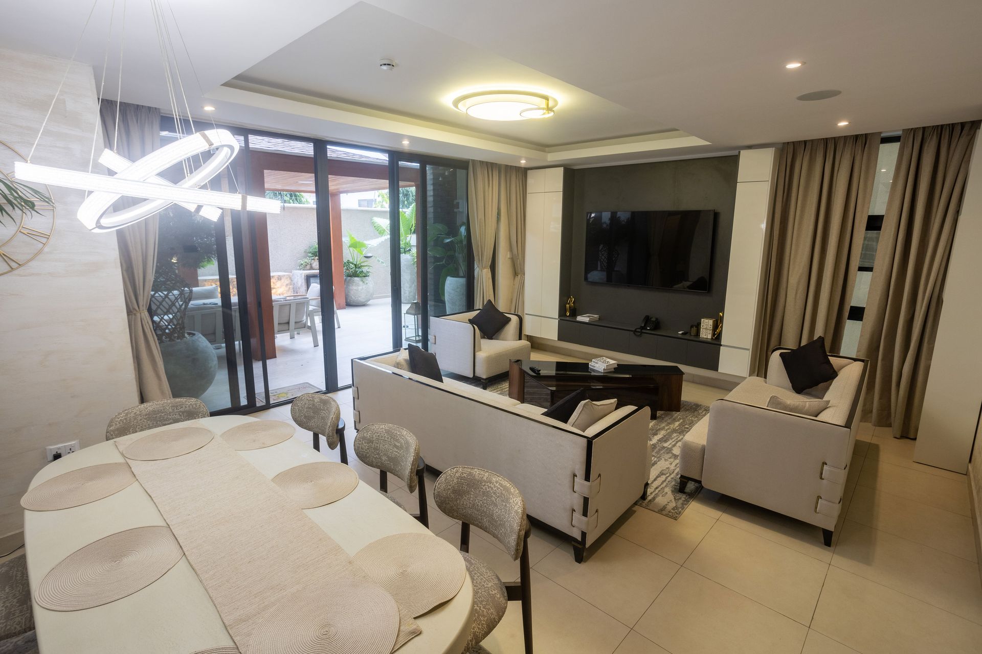 Modern living room with white furniture, wall-mounted TV, and sliding glass doors to a balcony.