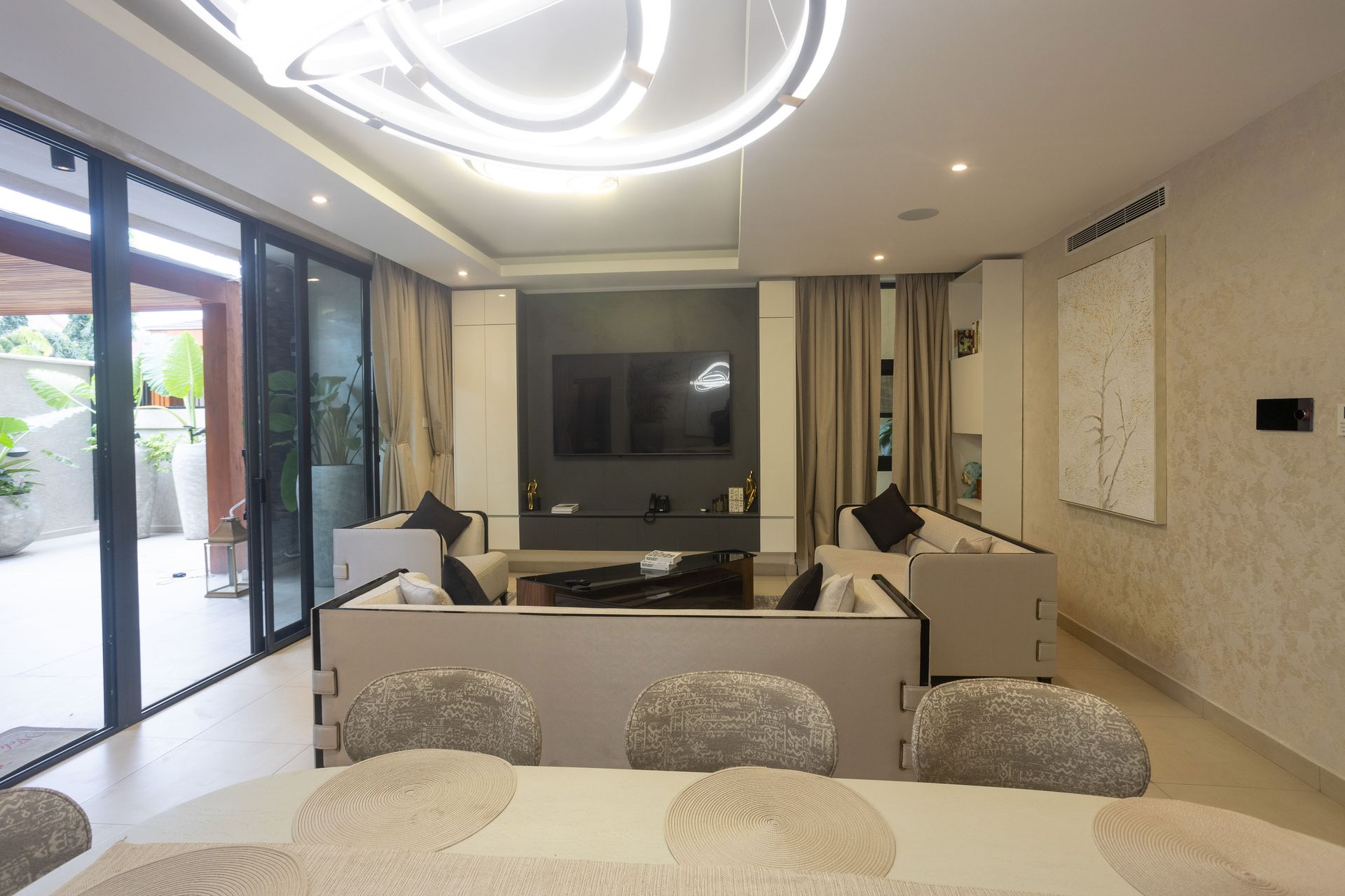 Modern living room with white furniture, TV wall, large sliding glass doors, and ceiling lights
