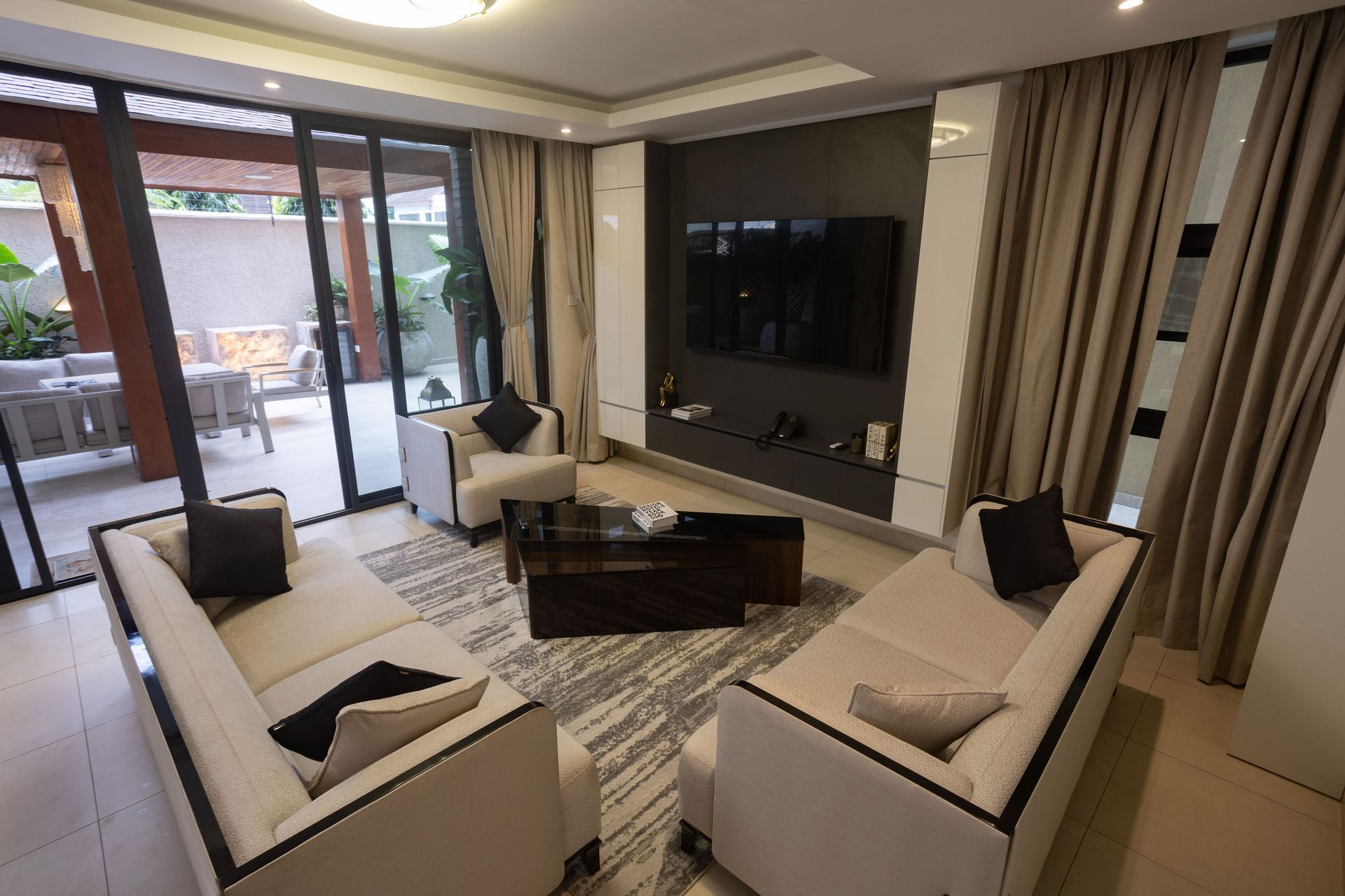 Modern living room with beige sofas, wall-mounted TV, and sliding glass doors to a patio.