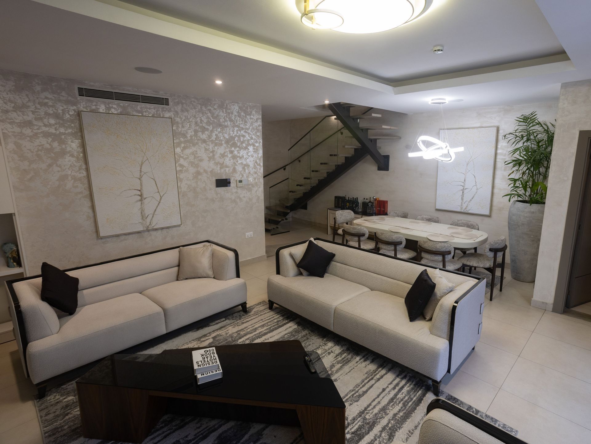 Modern living room with beige sofas, black coffee table, staircase, and patterned rug