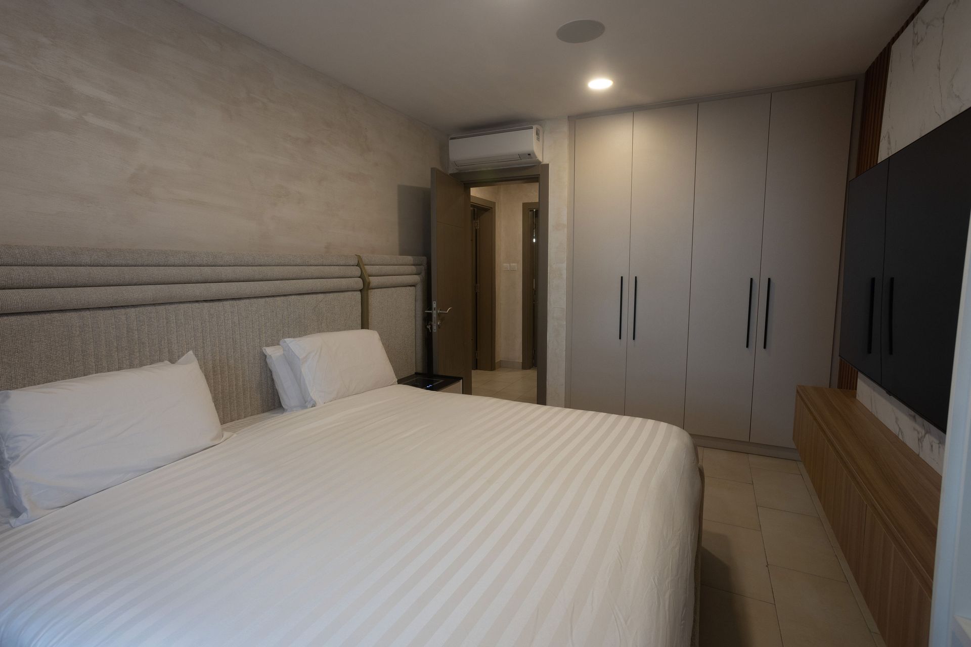 Modern bedroom with a neatly made white bed, built-in wardrobe, and wall-mounted TV