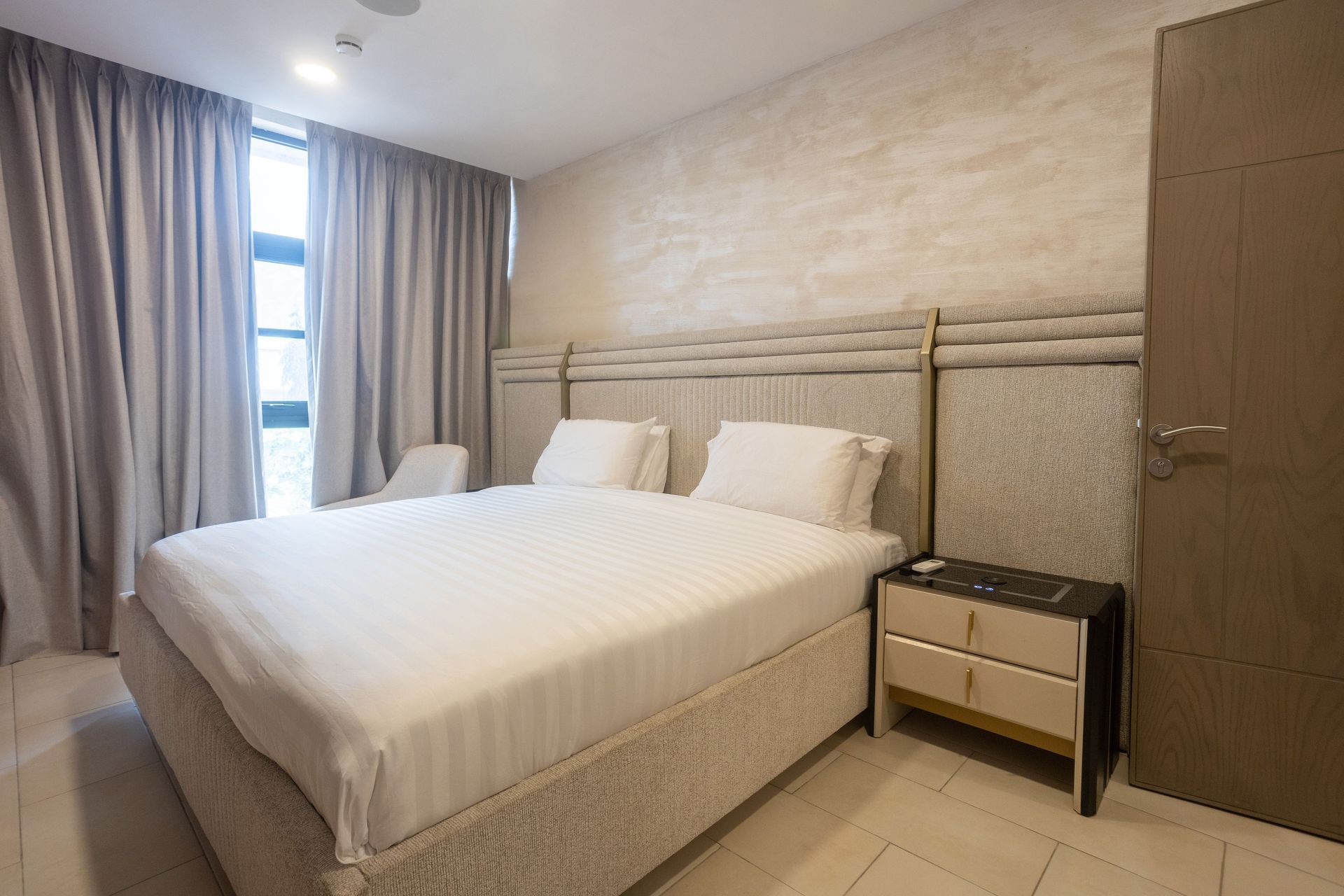 Modern bedroom with a white bed, beige walls, curtains, bedside table, and wardrobe