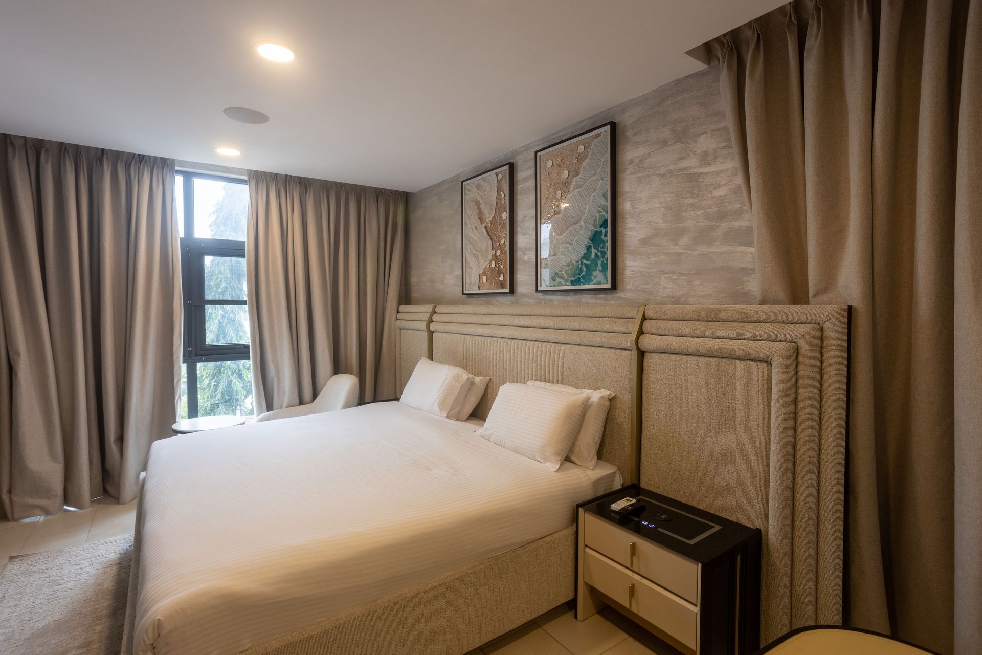 Modern bedroom with a white bed, beige curtains, and framed wall art near a window