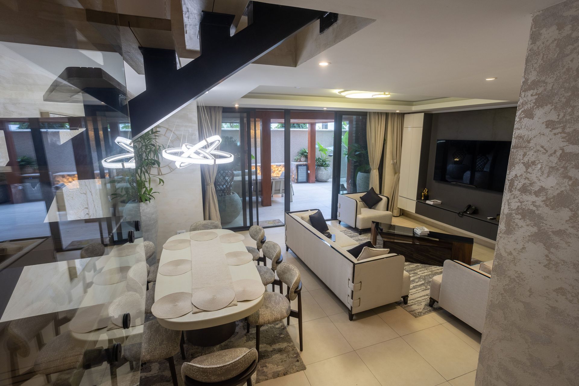 Modern open-plan living and dining room with white furniture, staircase, and large windows