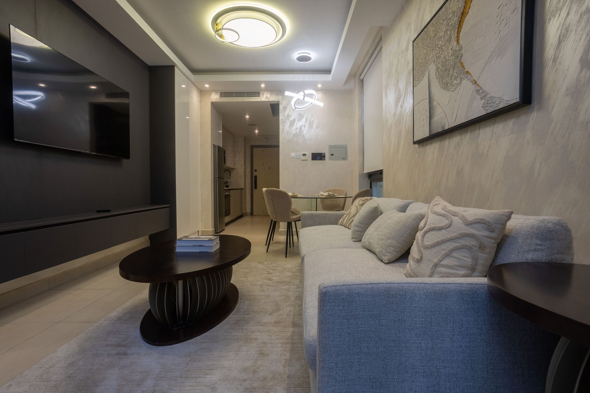 Modern living room with gray sofa, coffee table, wall-mounted TV, and warm ceiling lights