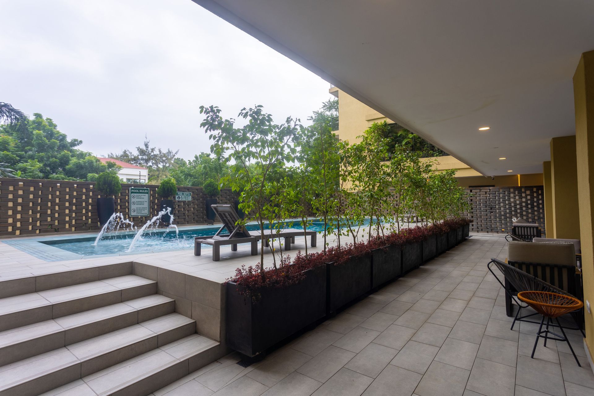 Covered pool deck with steps, lounge chairs, and a row of planters beside the water.