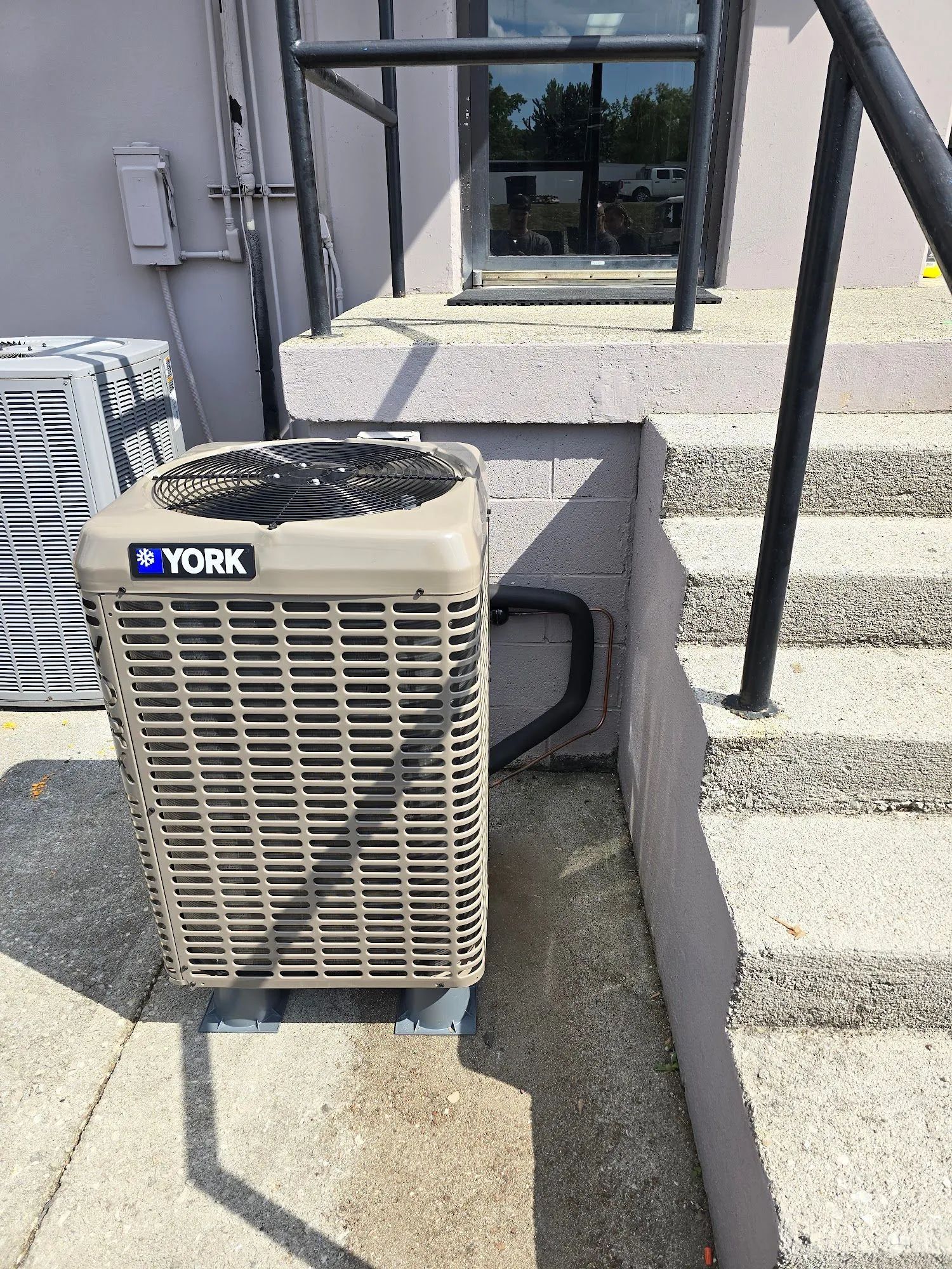 YORK air conditioner unit beside a building wall and steps on a concrete patio