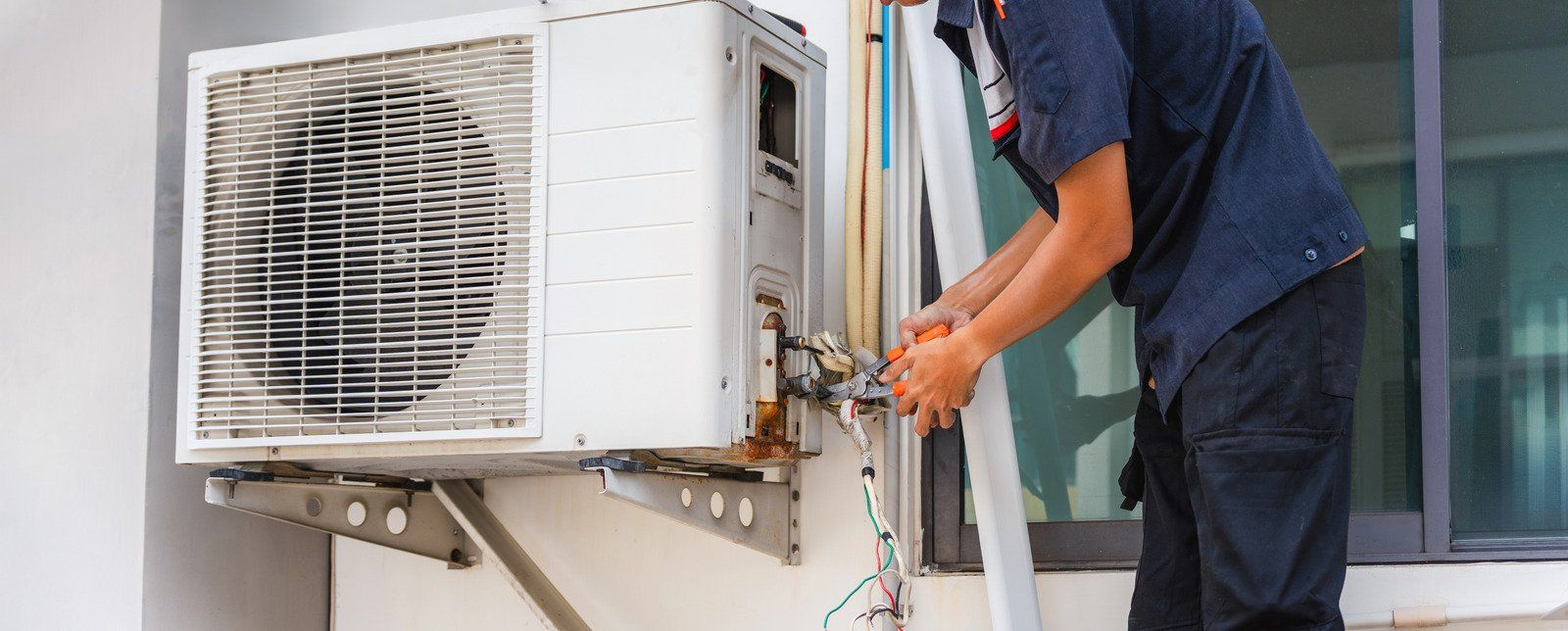 Technician adjusting an outdoor air conditioner unit with tools near a window