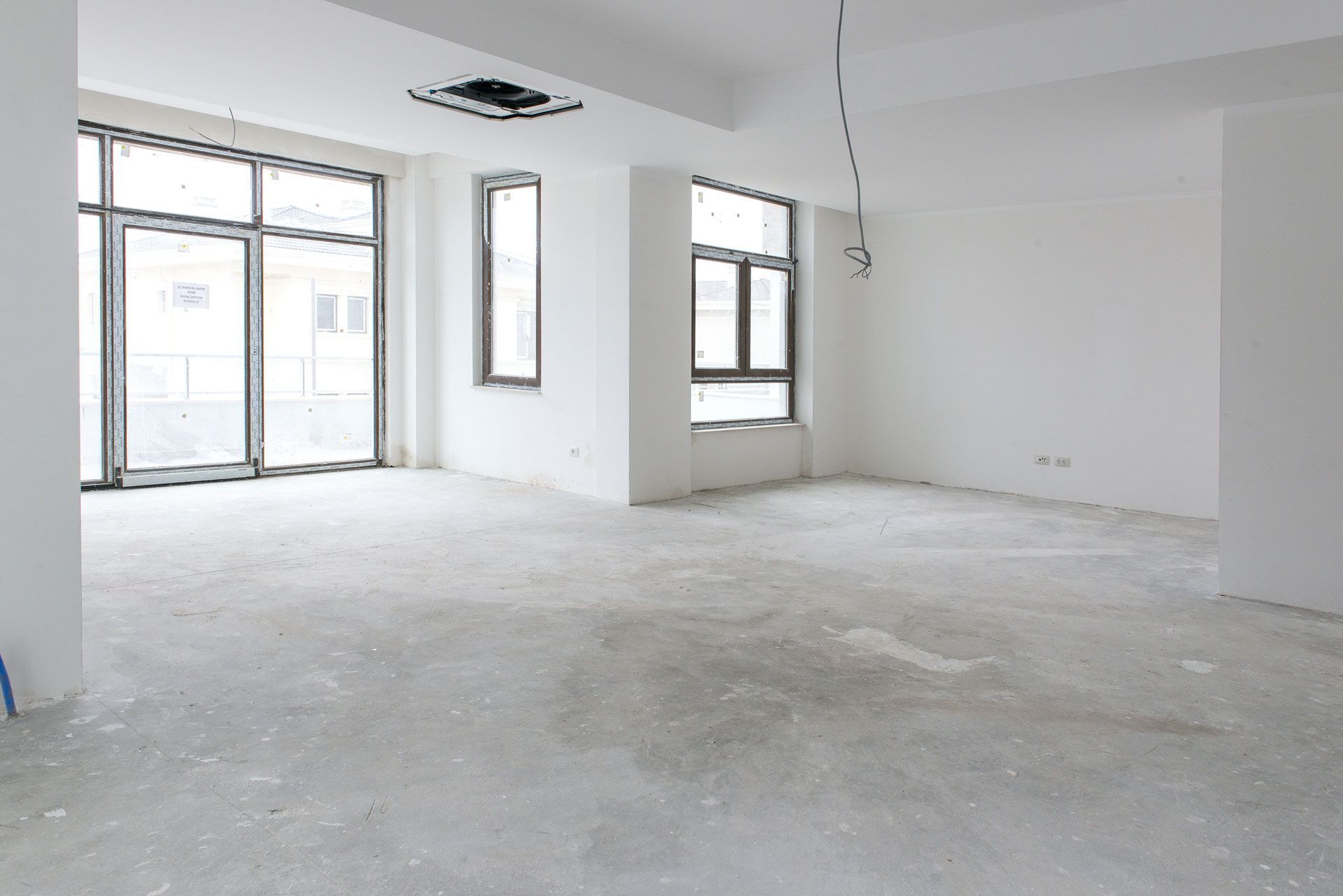 Empty room with large windows, unfinished flooring, and exposed electrical wires.