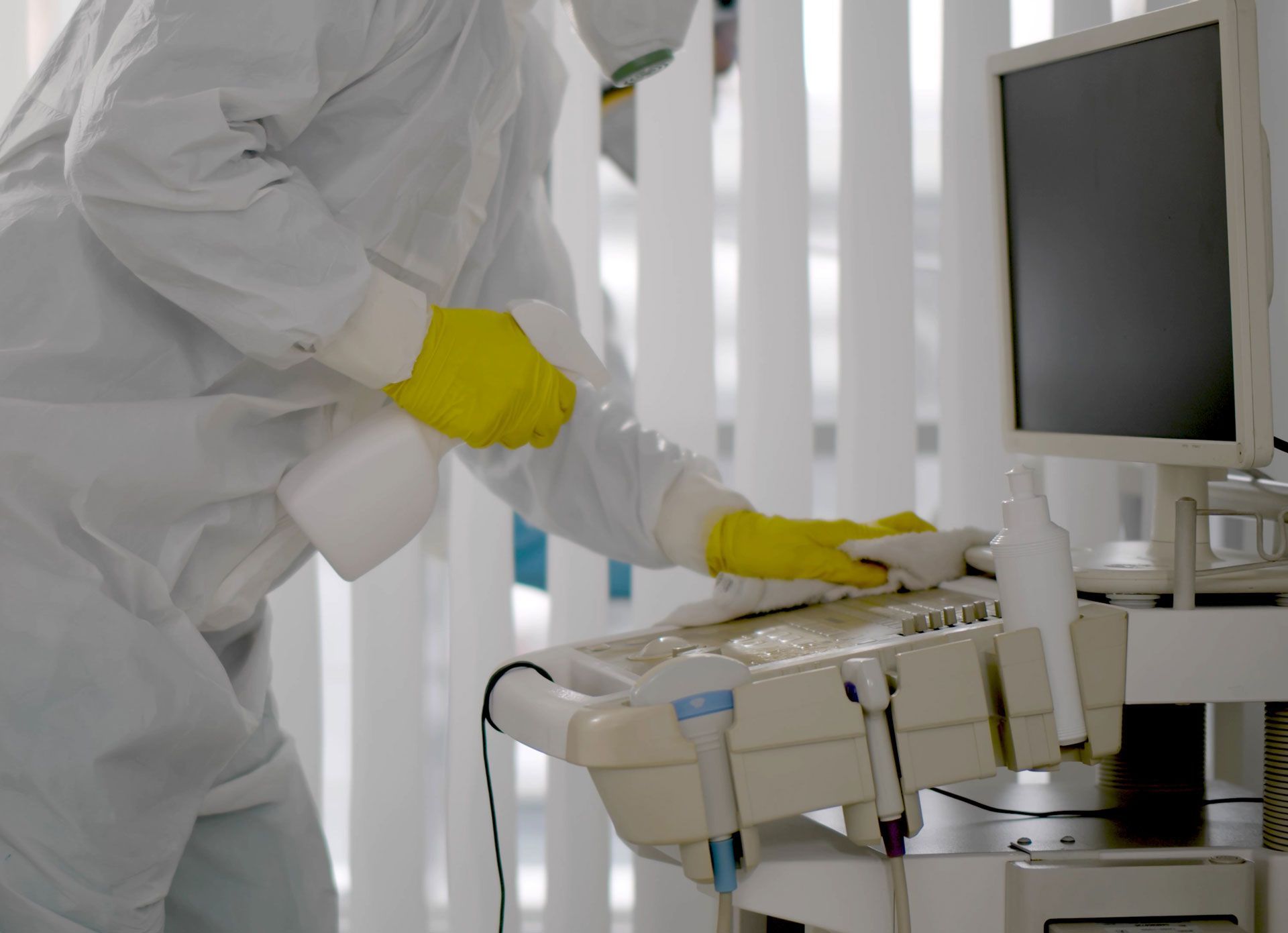 Person in white protective suit sanitizing medical equipment with yellow gloves.