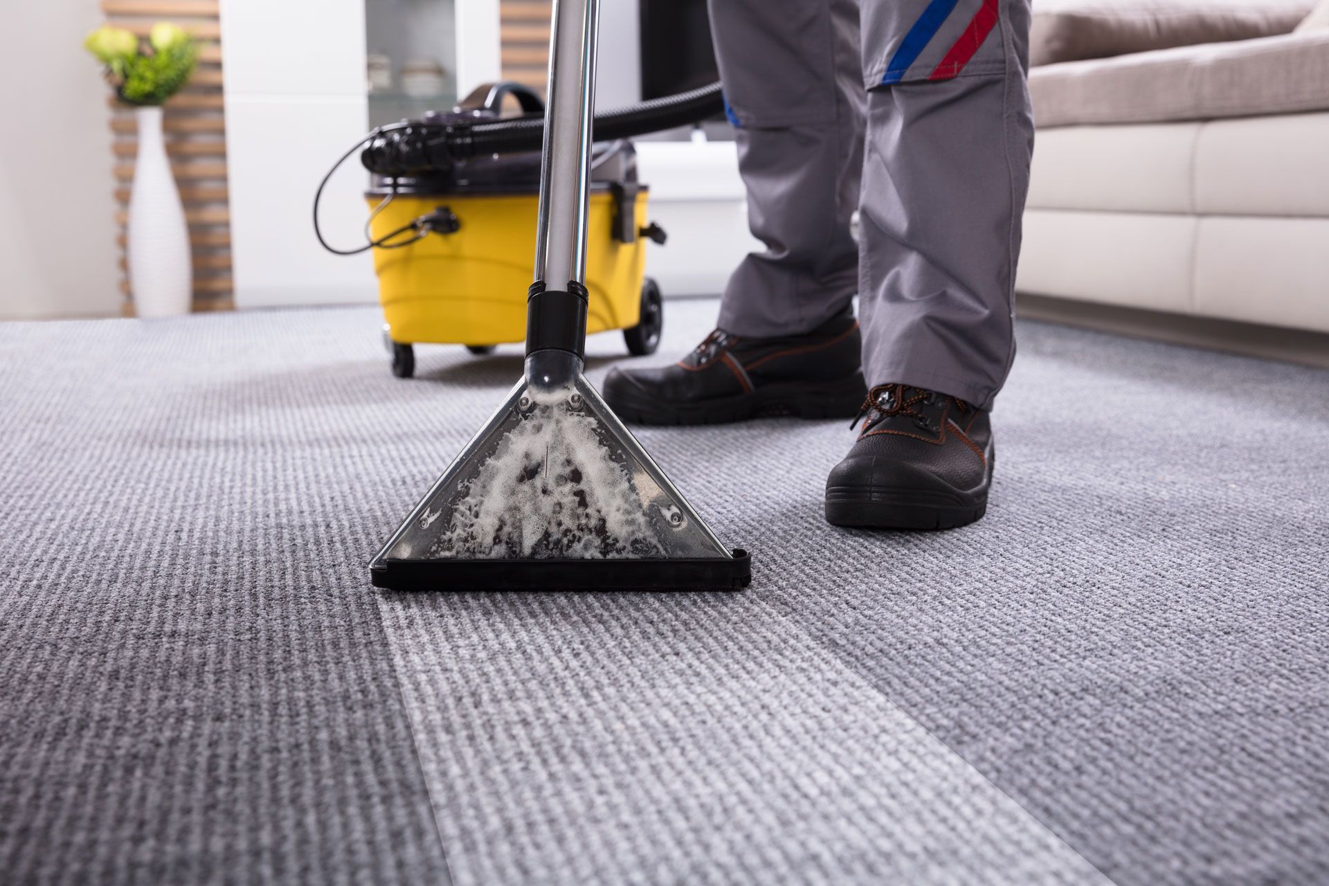 Person cleaning carpet with a yellow vacuum.