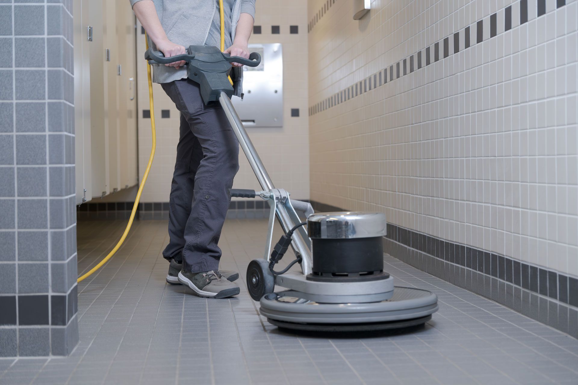Person operating a floor buffer in a tiled bathroom.