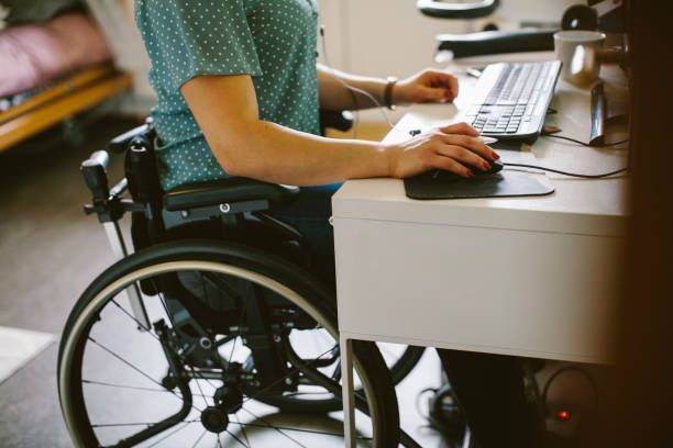 A woman in a wheelchair is sitting at a desk using a computer.