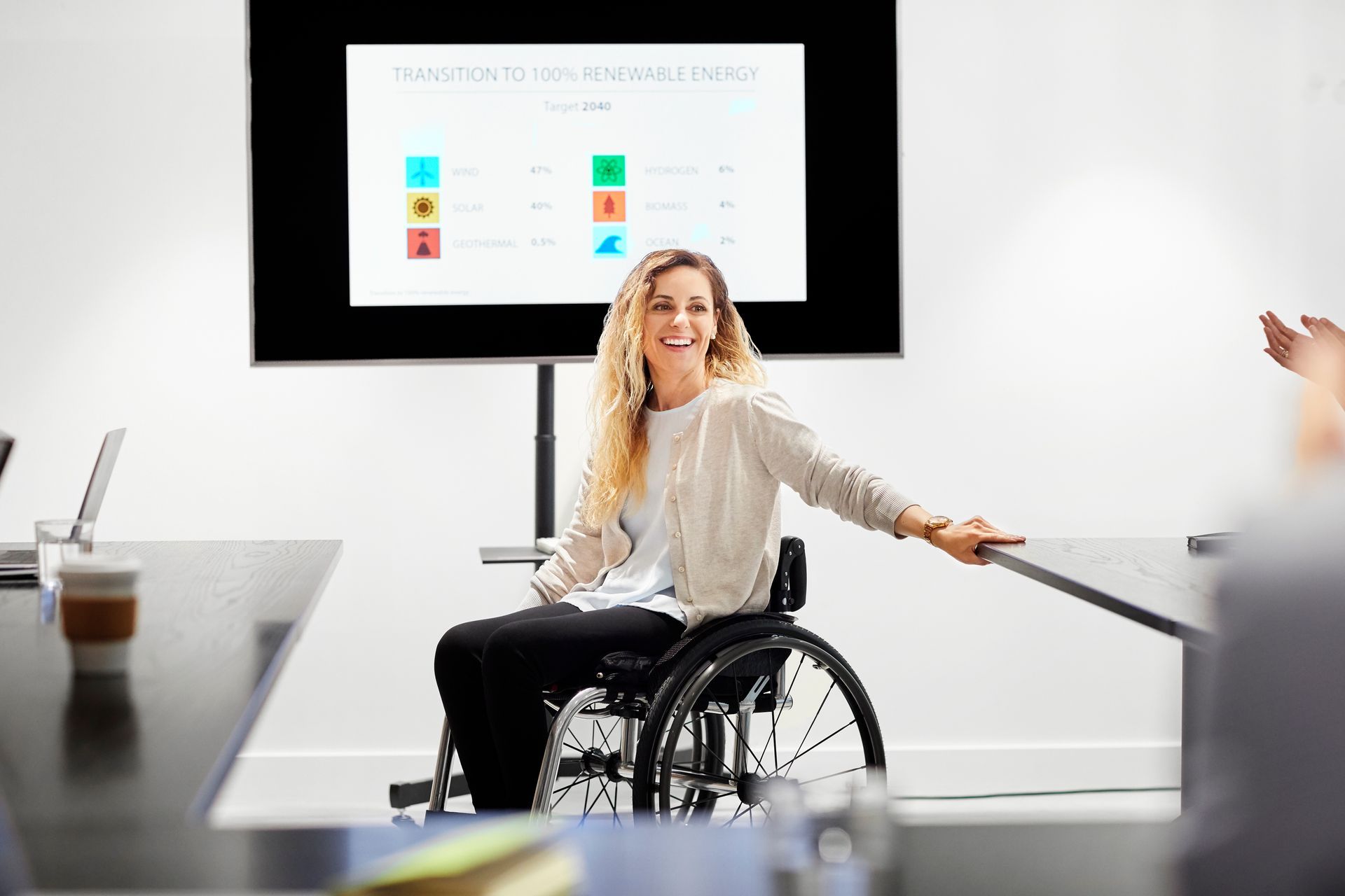 A woman in a wheelchair is sitting at a table in front of a screen.