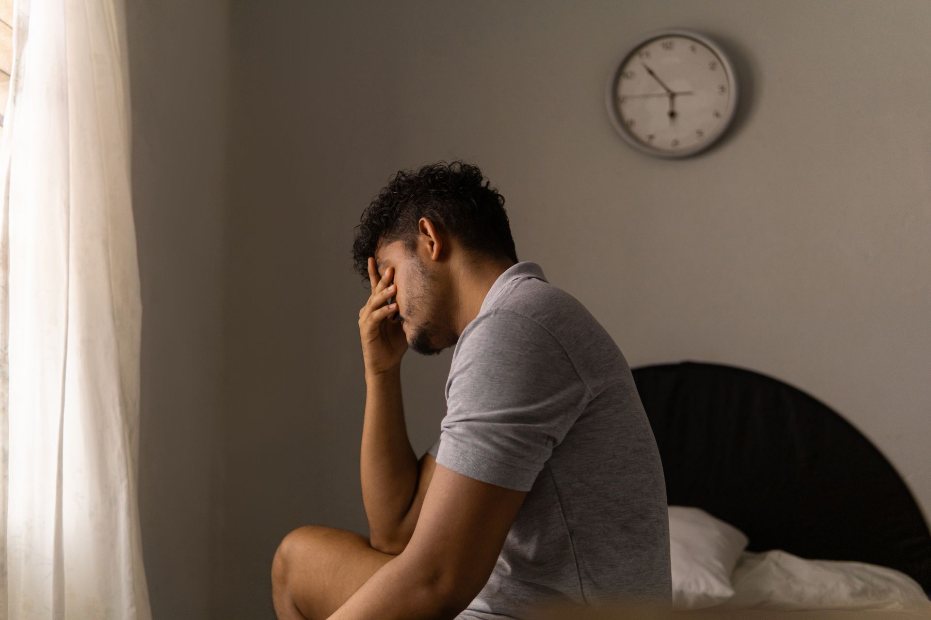 A man is sitting on a bed with his head in his hands.
