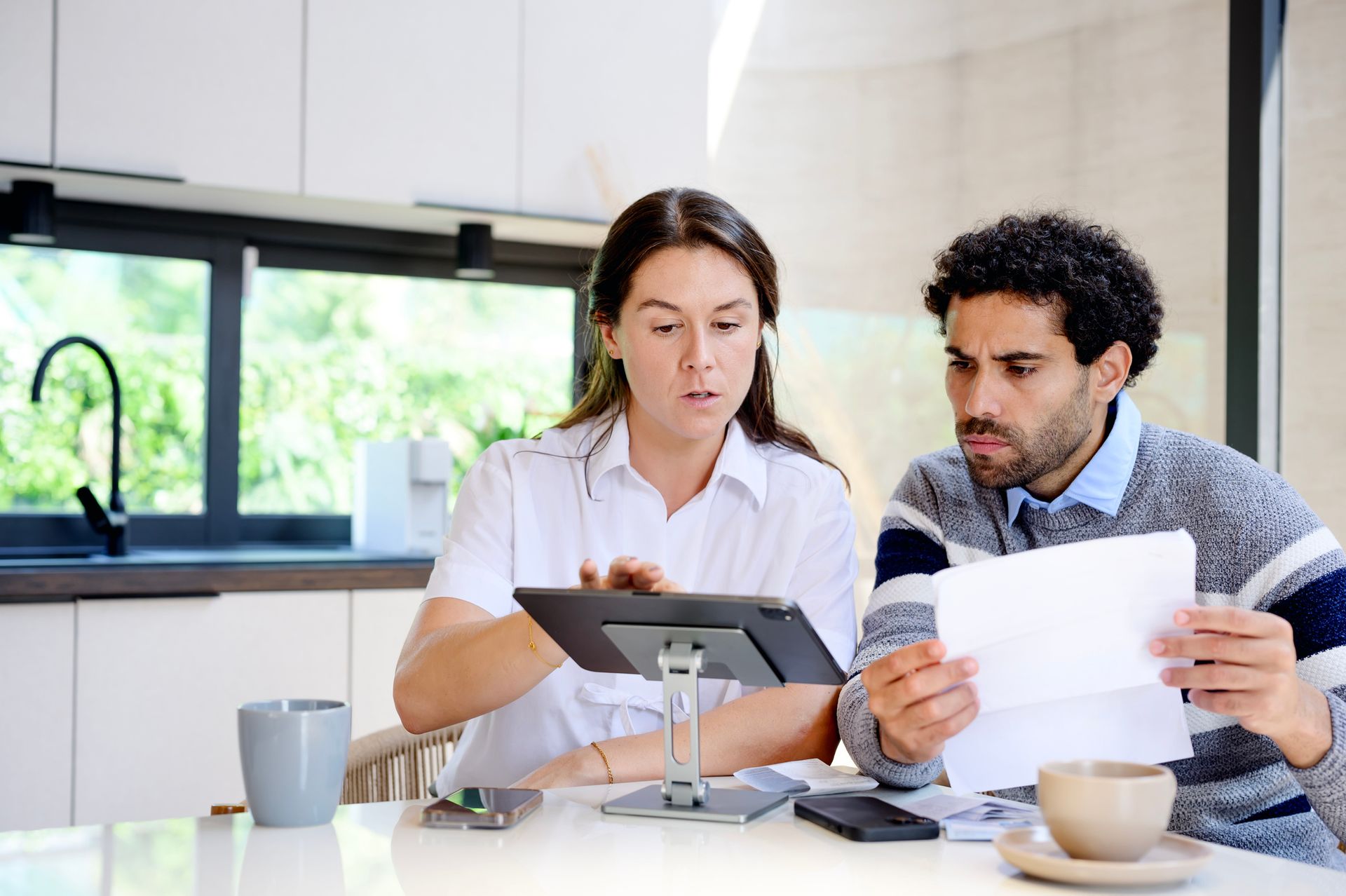 A man and a woman are sitting at a table looking at papers and a tablet. A man and a woman are sitting at a table looking at papers and a tablet.