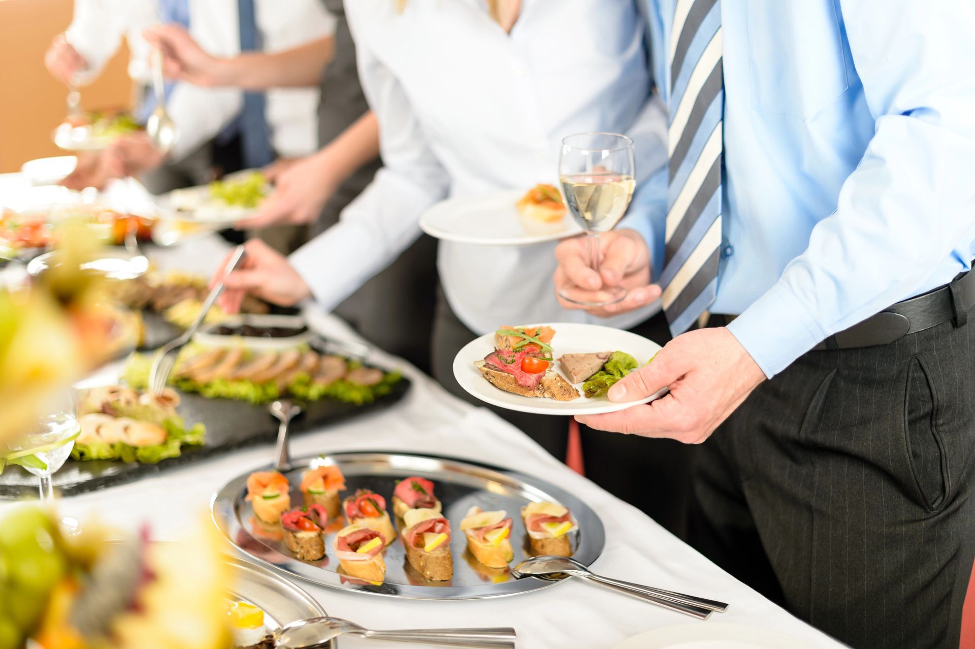 Un grupo de personas están de pie alrededor de una mesa de buffet comiendo comida.