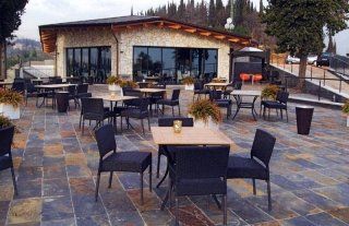 Patio esterno del ristorante con tavoli e sedie, di fronte a un edificio con ampie finestre.
