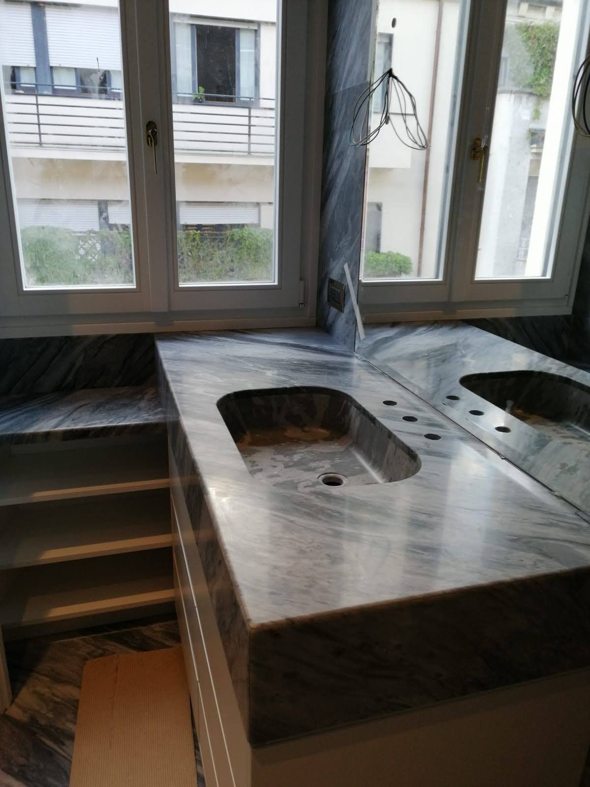 Mobile bagno con piano in marmo, lavandino e finestra con vista sugli edifici.