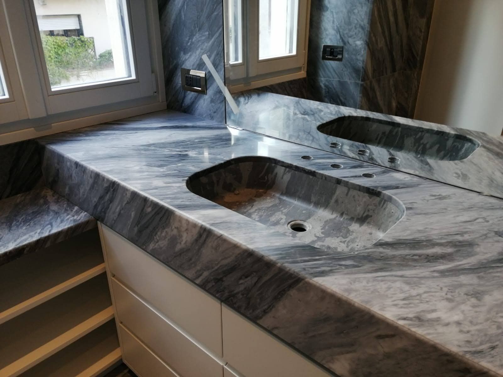 Piano di lavoro in marmo grigio e bianco con lavandino incorporato e finestra sullo sfondo.