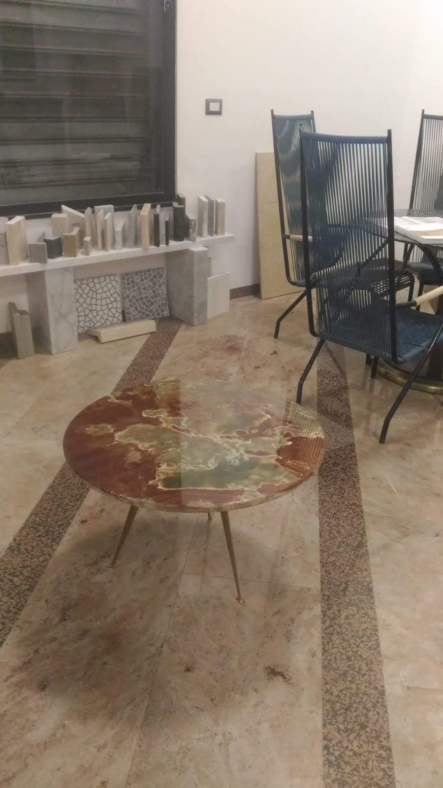 Tavolino rotondo con disegno di una mappa, su un pavimento piastrellato, con sedie e uno scaffale bianco sullo sfondo.