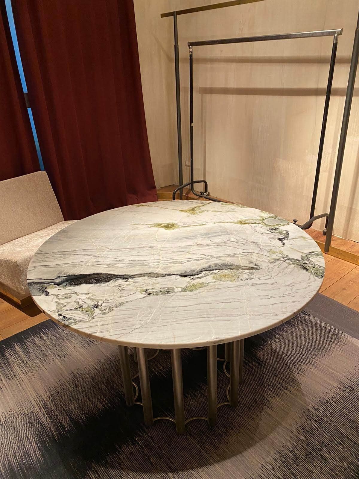 Tavolo rotondo in marmo con dettagli dorati e base in metallo, su un tappeto fantasia.