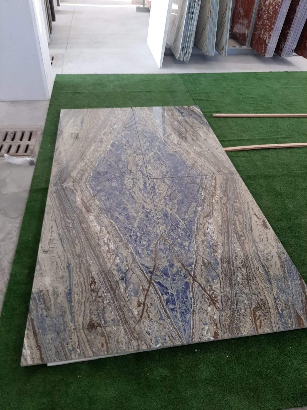 Grande lastra di pietra venata di blu, marrone e bianco esposta su un manto erboso verde.