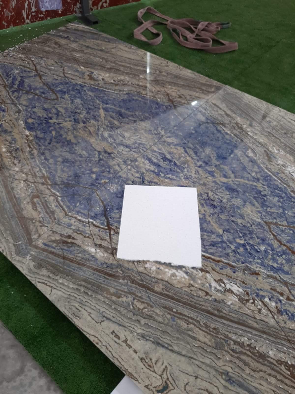 Lastra di pietra marmorizzata blu e marrone con un campione quadrato bianco sulla parte superiore.