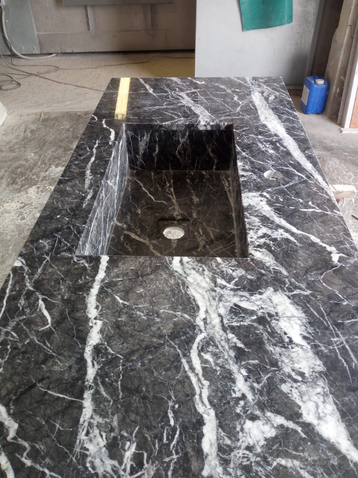 Piano di lavoro in marmo nero con lavabo rettangolare integrato, venature bianche.