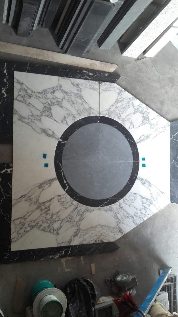 Pavimento in marmo geometrico con motivi bianchi e neri, tra cui un cerchio grigio centrale.