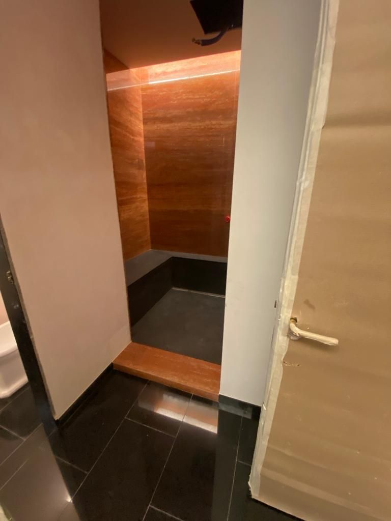 Una cabina doccia scura e chiusa, con pannelli in legno e pavimento piastrellato nero.