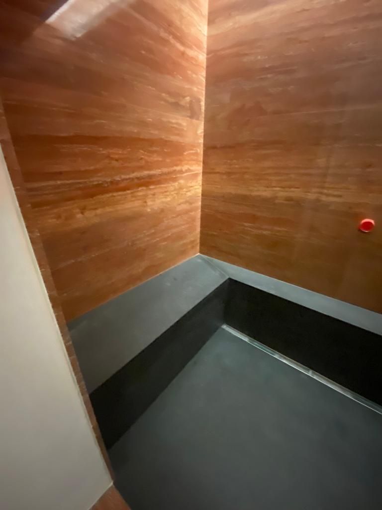 Box doccia angolare con base nera, pareti a strisce marroni e manopola rossa.