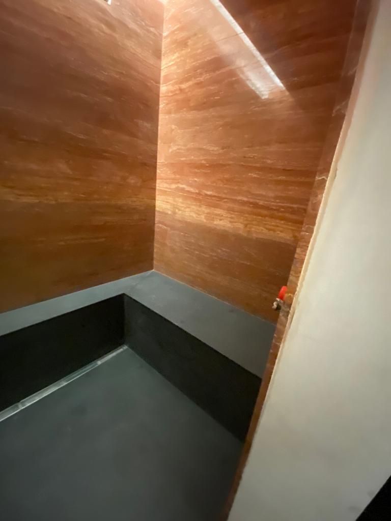 Una piccola doccia moderna con pareti rosso-marroni e panca e pavimento grigio scuro. Una porta bianca è parzialmente visibile.