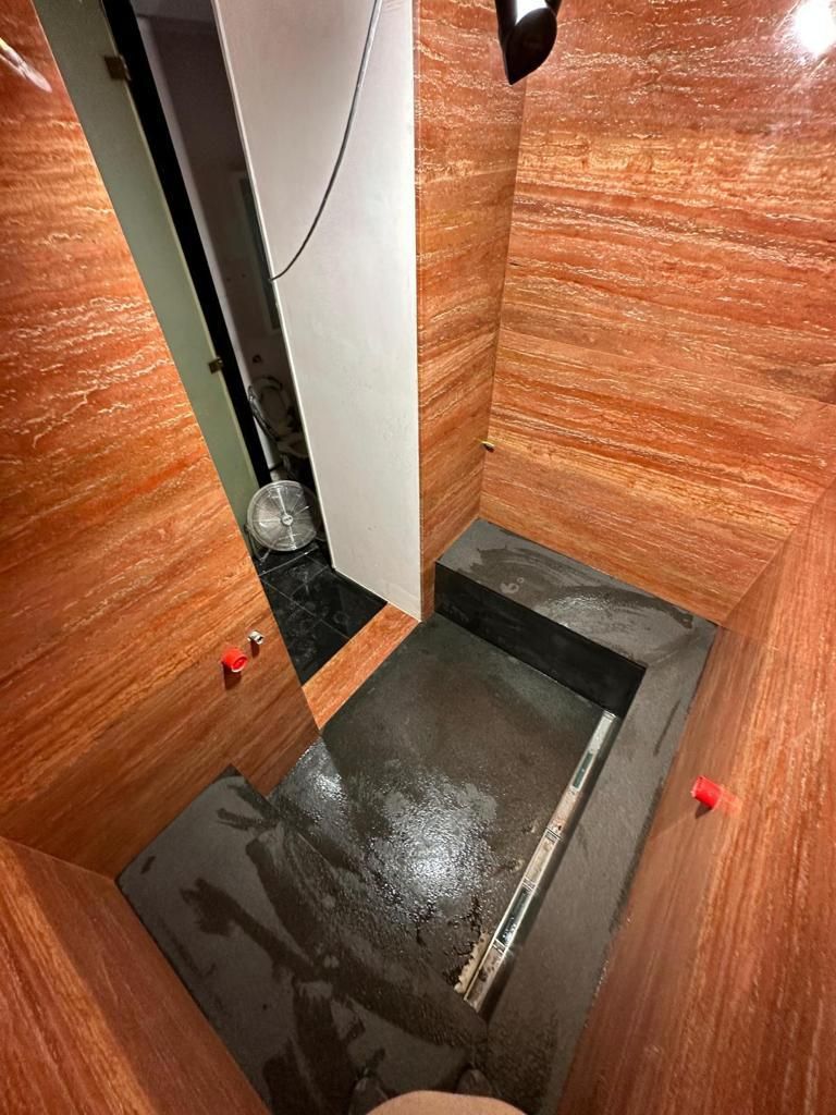 Stanza stretta, rivestita in legno, con pavimento scuro a gradini. Piccole manopole rosse.