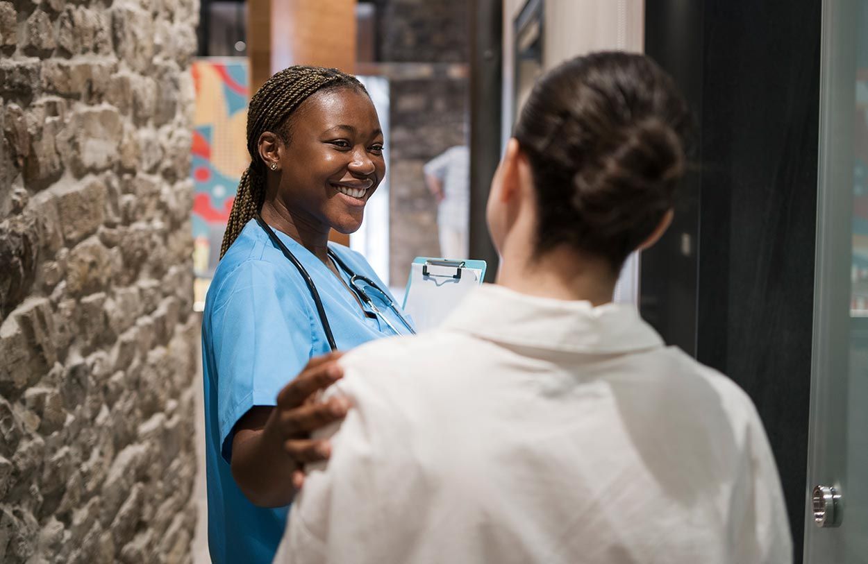 Two people smiling and talking in a hallway, one in a blue shirt and one in a white jacket.