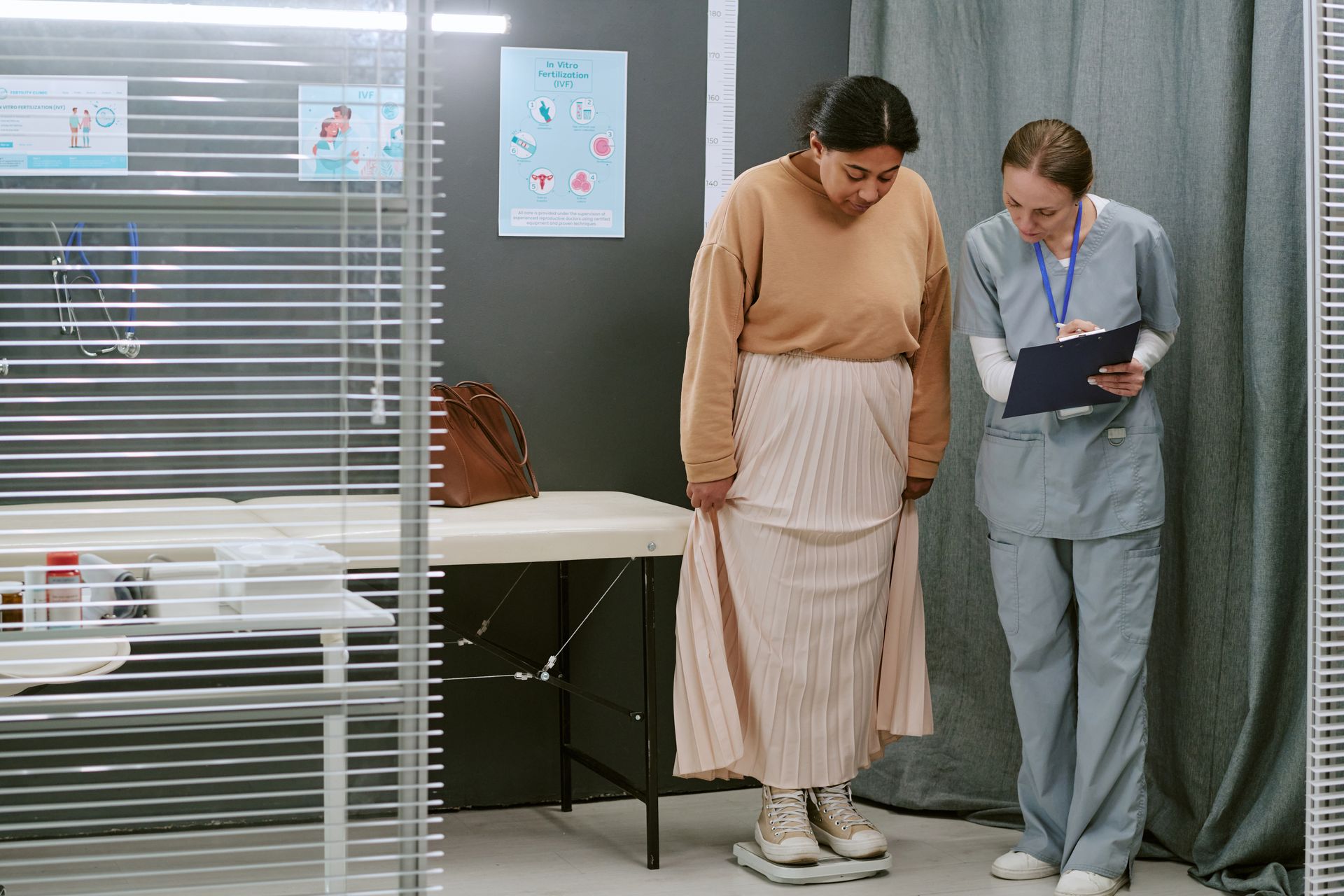 Two people in a clinic room reviewing paperwork beside an exam table and privacy curtain