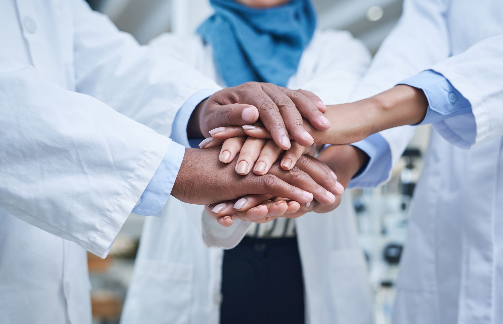 Hands stacked together in a team huddle, with people wearing white lab coats.