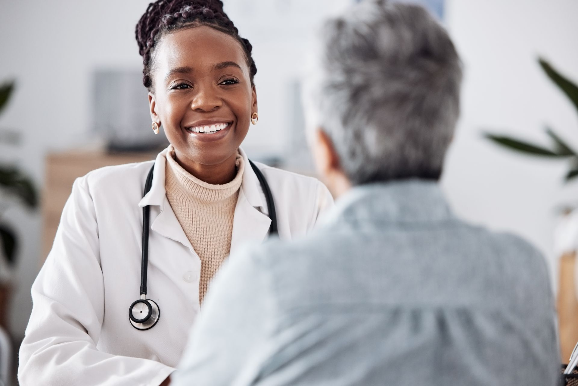 Smiling doctor in white coat speaking with a seated patient in a bright clinic office